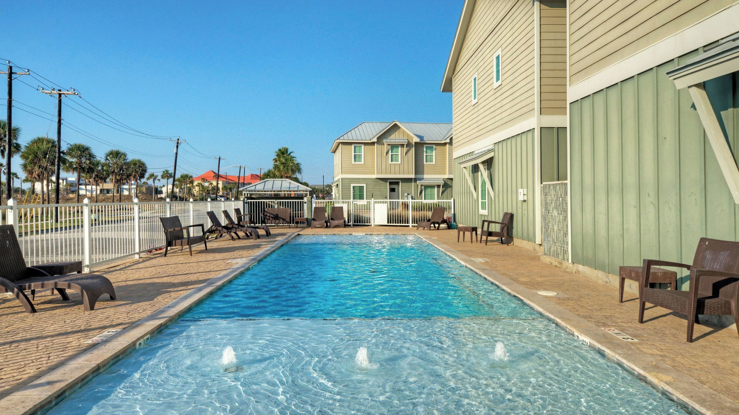 A swimming pool with lounge chairs, a fenced area, and a building with a green exterior.