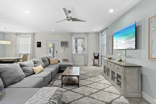 A modern living room with a grey sectional sofa, a wooden coffee table, and a large TV on the wall. - 30A Wave From It All by Avantstay Blue Mountain (Santa Rosa Beach)