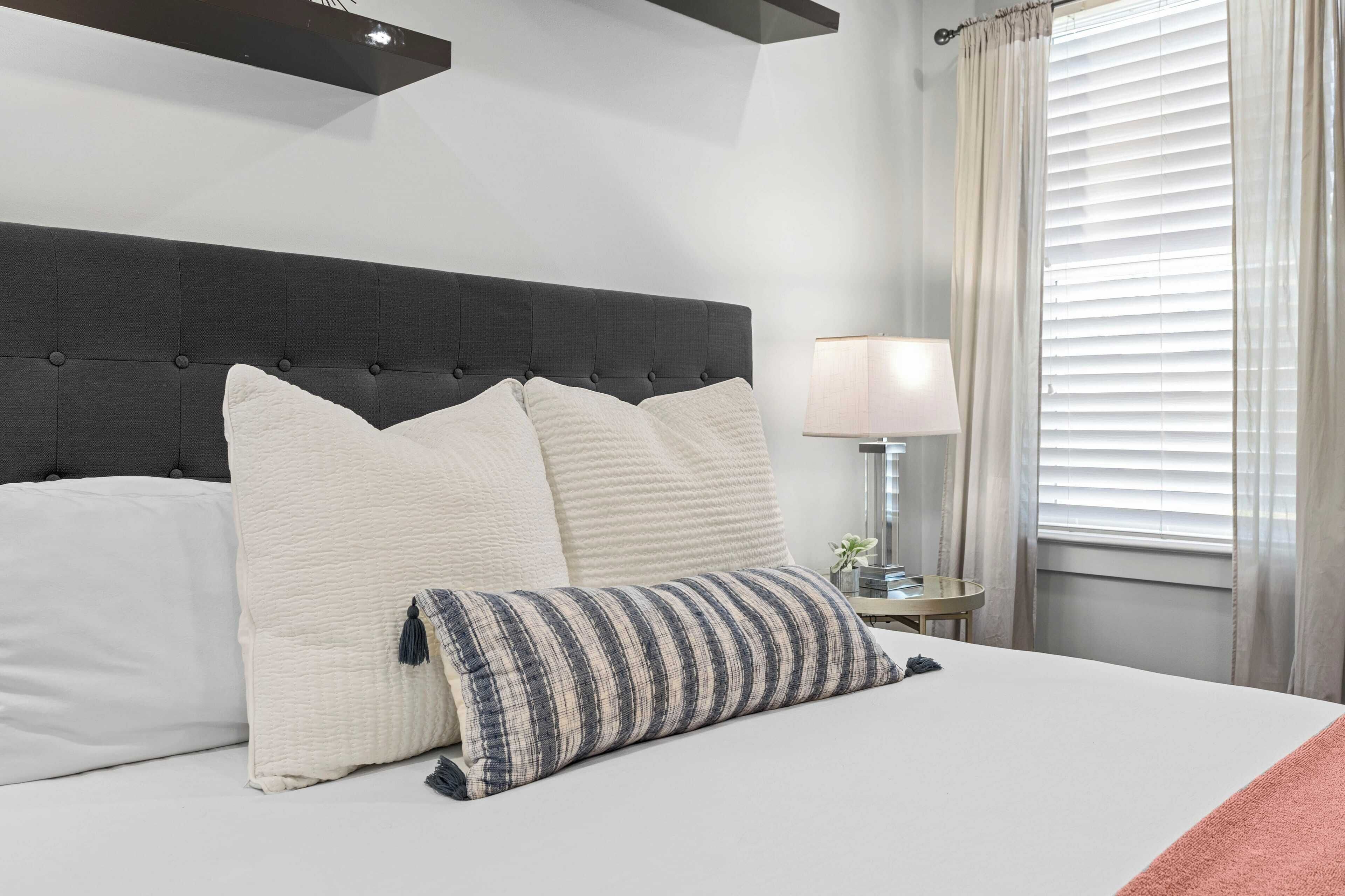 A neatly made bed with a dark headboard, white and striped pillows, and a bedside table with a lamp and a small plant.