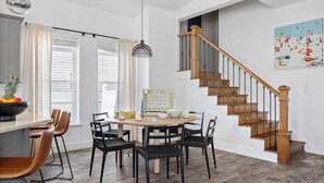 A dining area with a round table, black chairs, a fruit bowl, and a wooden staircase with a railing. - 7bdr w/ Private Pool, Hot Tub, Fire Pit, Walk to Beach Tidal Wave by Avantstay (Destin)