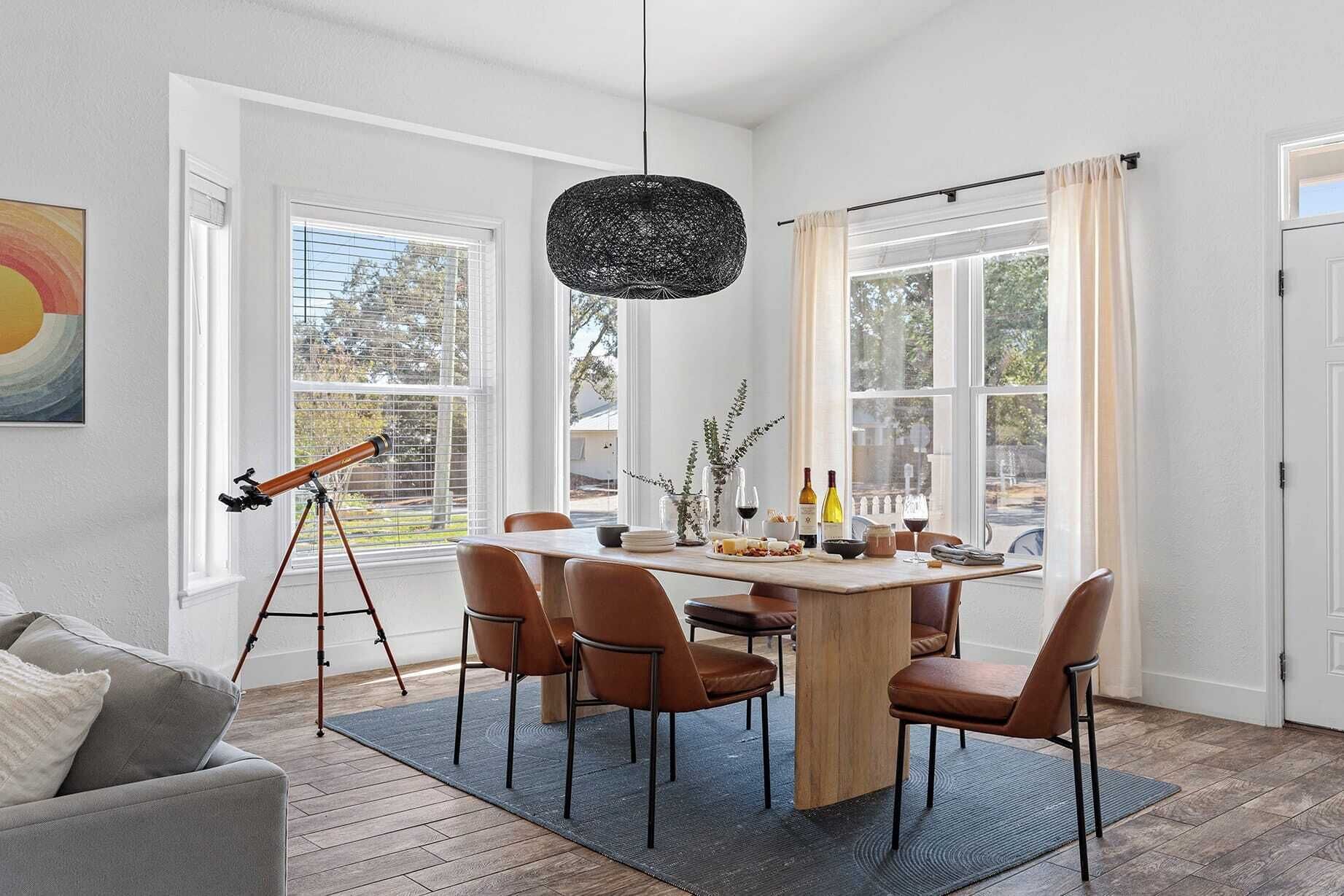 A dining area with a round table, six chairs, a telescope, and a hanging light fixture.