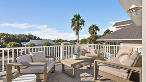 A wooden deck with outdoor furniture, a white railing, and a view of surrounding houses and palm trees. - 7bdr w/ Private Pool, Hot Tub, Fire Pit, Walk to Beach Tidal Wave by Avantstay (Destin)