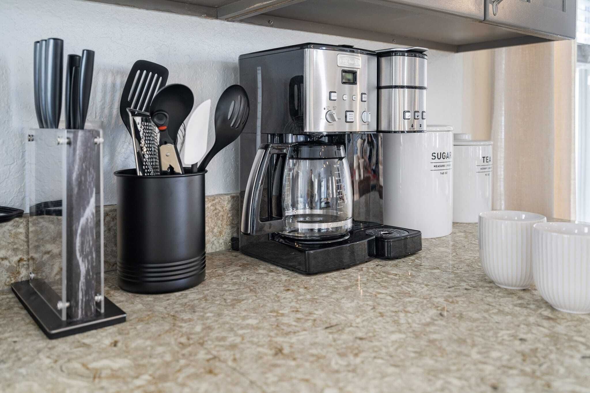Una cocina con cafetera, utensilios, y recipientes de azúcar y té.