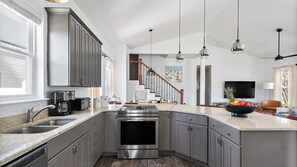 A modern kitchen with a large island, stainless steel appliances, and a view to the living area. - 7bdr w/ Private Pool, Hot Tub, Fire Pit, Walk to Beach Tidal Wave by Avantstay (Destin)