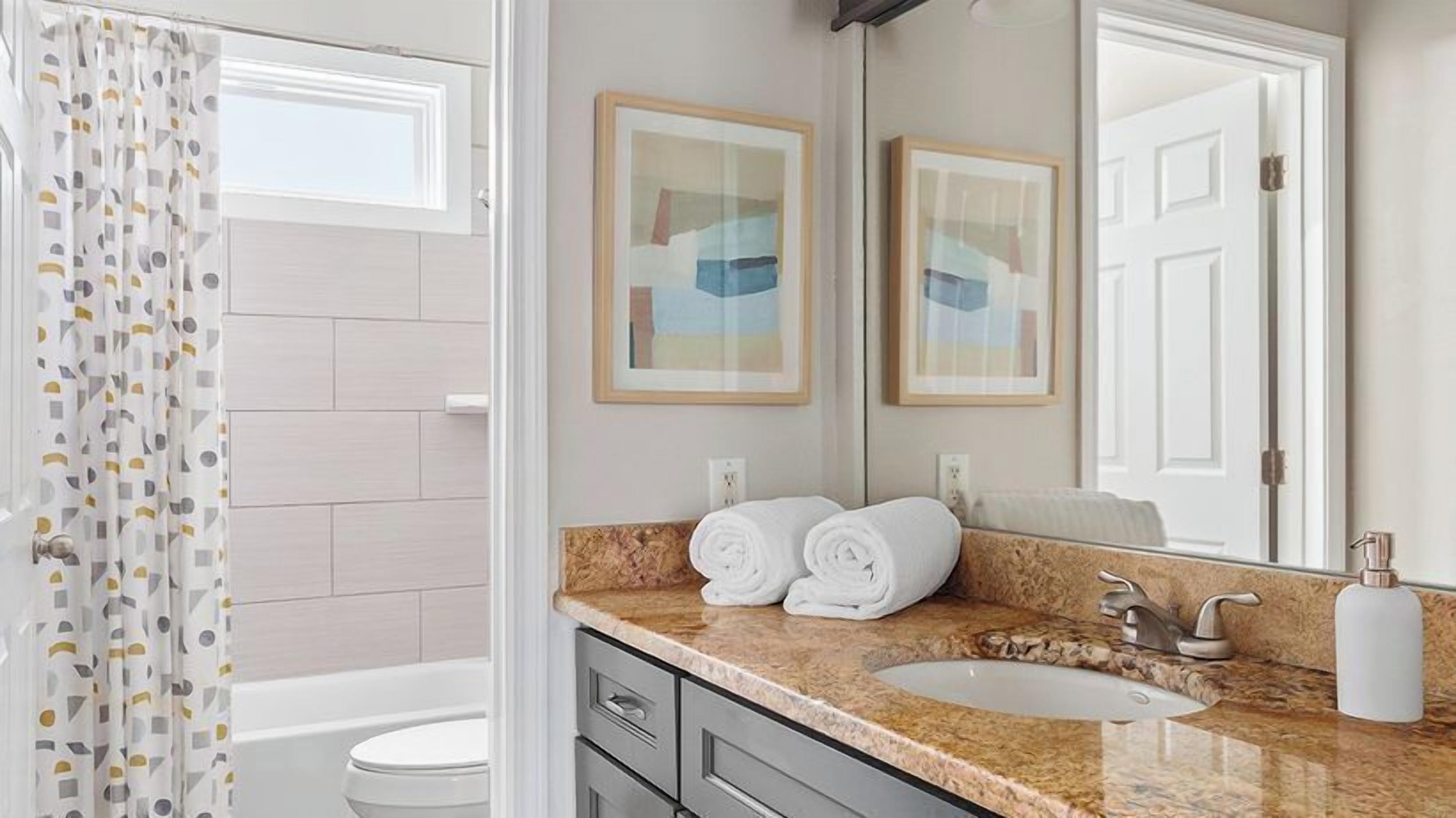A bathroom with a sink, mirror, towels, and a shower curtain.