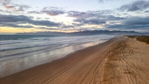A beach with a long stretch of sand, a calm sea, and distant mountains under a partly cloudy sky. - Mendel Manor by Avantstay Walk to Beach Large Deck Patio (Oceano)