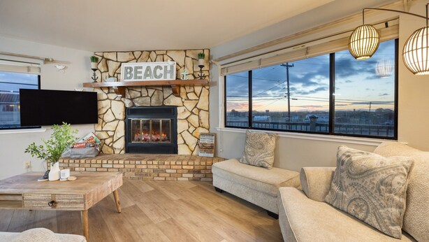 A cozy living room with a stone fireplace, a flat-screen TV, and a large window with a view. - Mendel Manor by Avantstay Walk to Beach Large Deck Patio (Oceano)