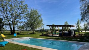Une piscine rectangulaire, avec une pergola en bois et des chaises en arrière-plan.