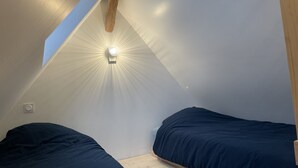 Une petite chambre mansardée, peu éclairée, avec deux lits et un plafond en pente.