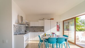 Moderni keittiö, jossa on valkoiset kaapit, marmoripintainen välitila ja ruokailutila, jossa on turkoosinsiniset tuolit.