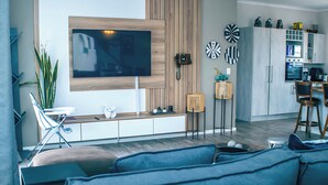 A modern living room with a large flat-screen TV, a sofa, a coffee table, and a dining area with chairs and a small table. - Spacious 3BR Family Haven in Walvis Bay – 30 Min to Swakopmund! Self-Catering (Walvis  Bay)