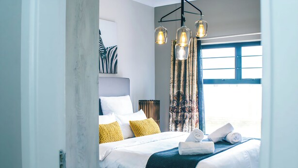 A hotel room with a bed, pillows, a window with curtains, and hanging light fixtures. - Spacious 3BR Family Haven in Walvis Bay – 30 Min to Swakopmund! Self-Catering (Walvis  Bay)