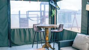 A room with a round wooden table, two bar stools, a wicker sofa, and a large window with a view. - Spacious 3BR Family Haven in Walvis Bay – 30 Min to Swakopmund! Self-Catering (Walvis  Bay)
