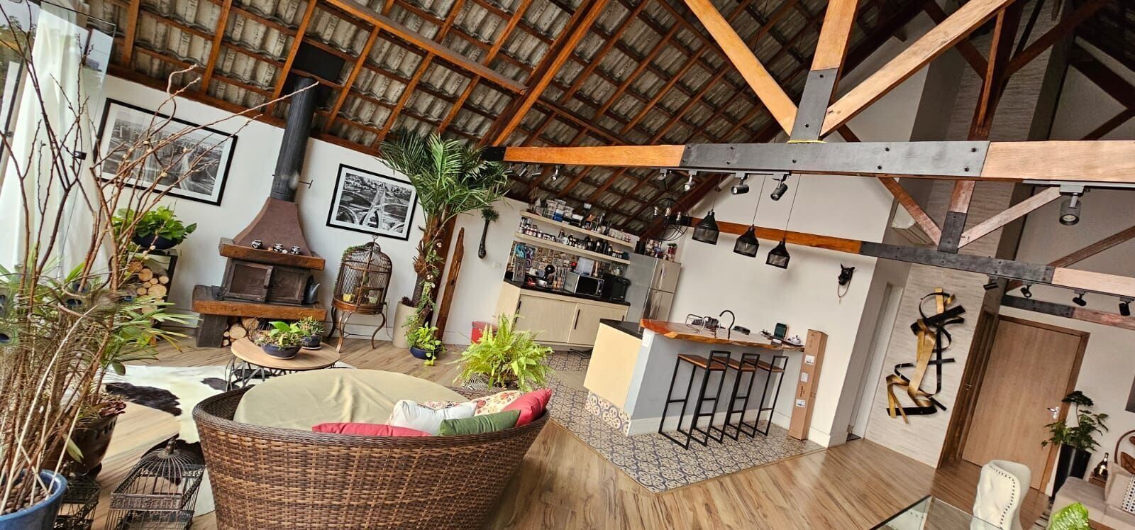 Um amplo loft com pé direito alto, vigas de madeira aparentes, um sofá de vime grande, um espaço de jantar e uma cozinha com banquetas.