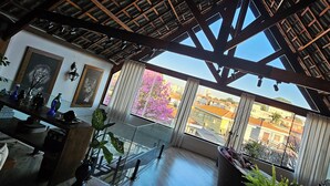 A spacious room with a high ceiling, large windows, and a balcony with a view of the city. - Chalé Ateliê Poder das Pedras (São Paulo)