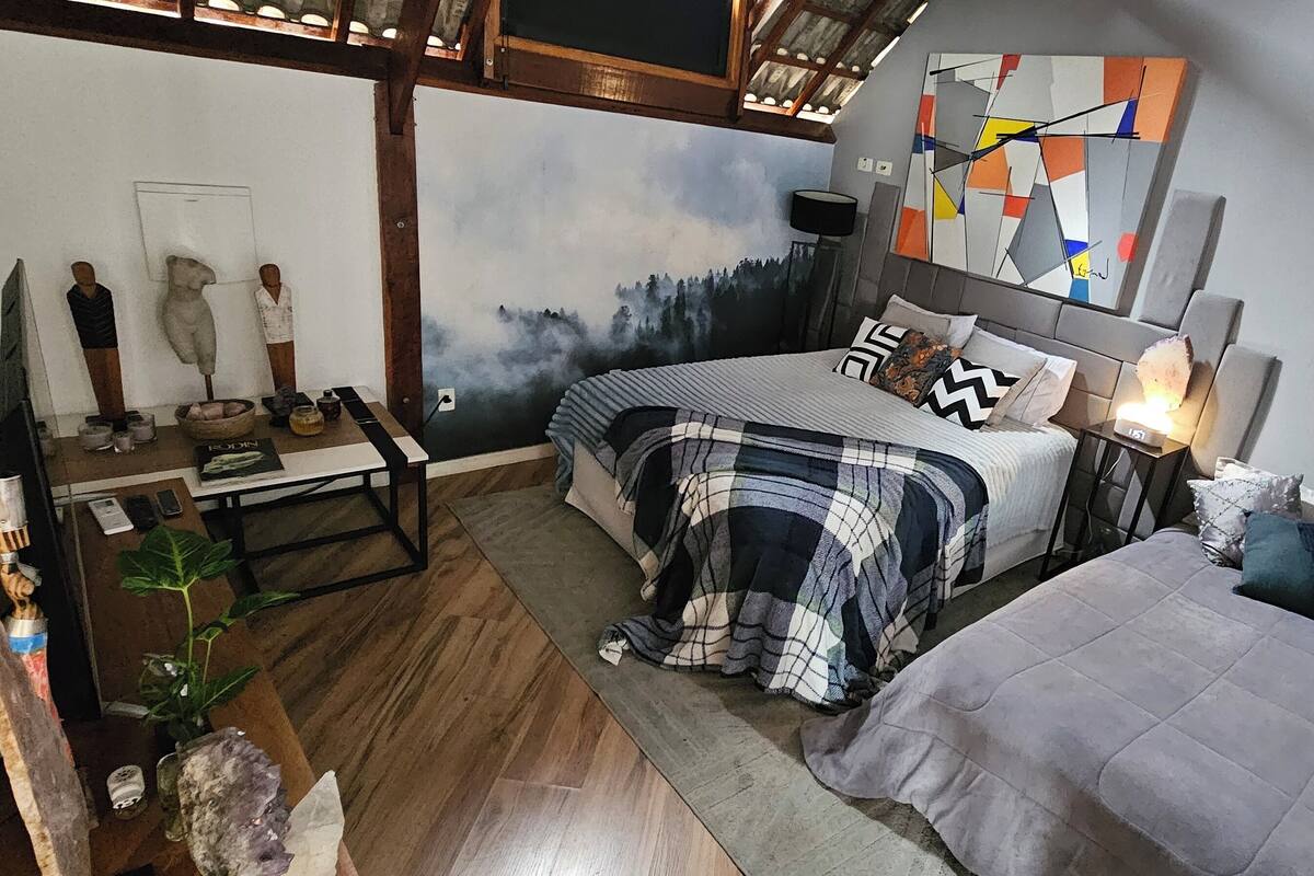 A bedroom with a bed, bedside tables, a nightstand, a lamp, a mirror, and a painting on the wall.