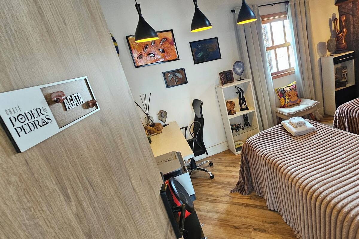 A hotel room with two beds, a desk, a chair, and a shelf with various items.
