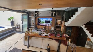 A modern living room with a large TV, wooden furniture, and a view of a pool. - Chalé Ateliê Poder das Pedras (São Paulo)