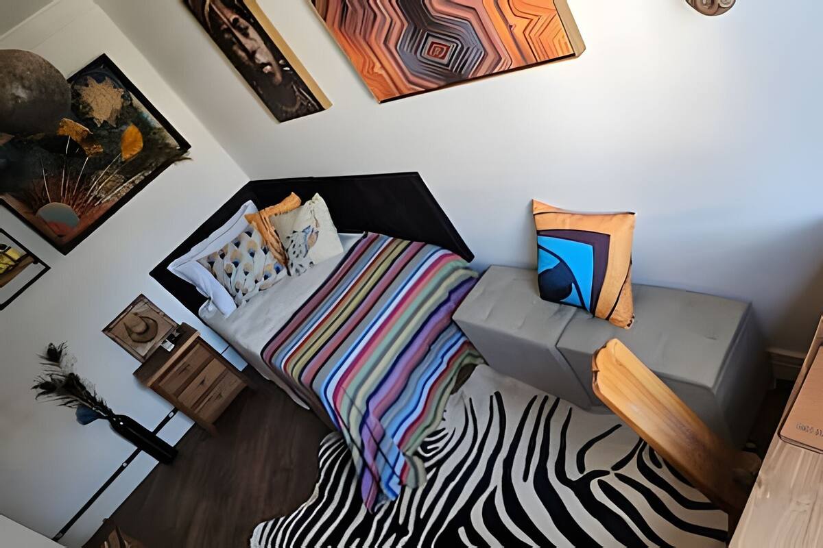 A compact bedroom with a bed, a bedside table, a chair, and a zebra-patterned rug.