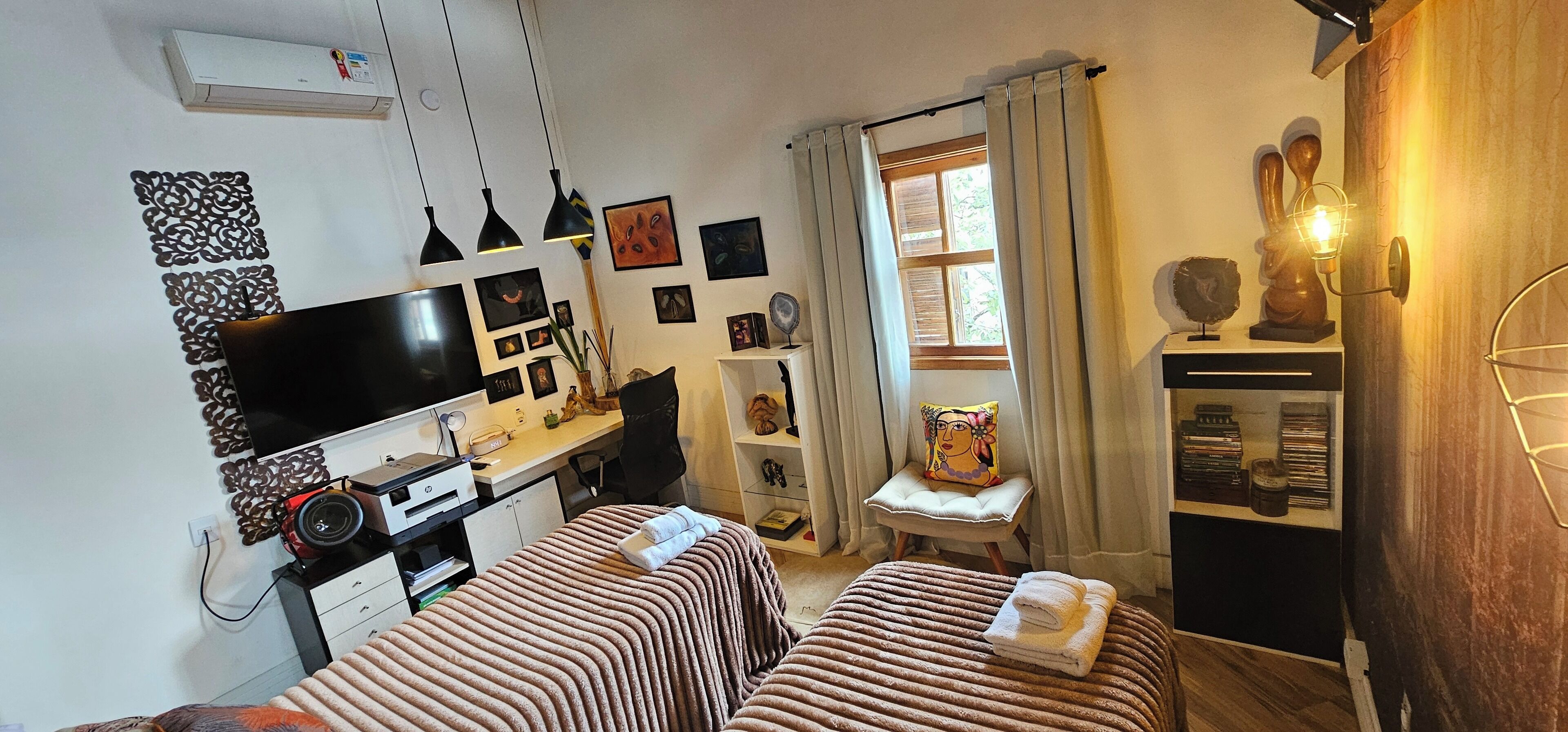 A compact bedroom with two beds, a desk with a computer, a TV, and a window with curtains.