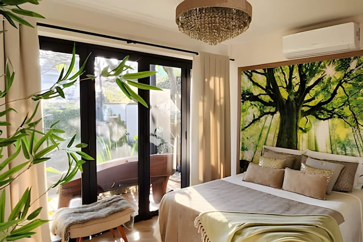 A bedroom with a bed, a large window, a tree mural, and a ceiling light fixture.