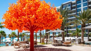 Un árbol con hojas de color naranja brillante frente a un hotel de varios pisos y balcones.