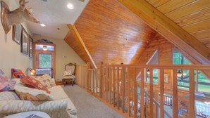 A cozy attic bedroom with a sloped wooden ceiling, a view of the outdoors, and a mounted deer head on the wall. - Tropical Room at Cabin on the Lake (Lake Helen)