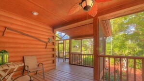 A log cabin with a wooden deck, a table with chairs, and a view of the surrounding forest. - Tropical Room at Cabin on the Lake (Lake Helen)