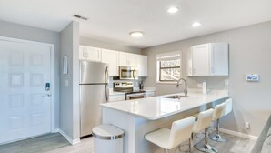 Une cuisine moderne avec des meubles blancs, des appareils en acier inoxydable et un îlot central doté de tabourets de bar.
