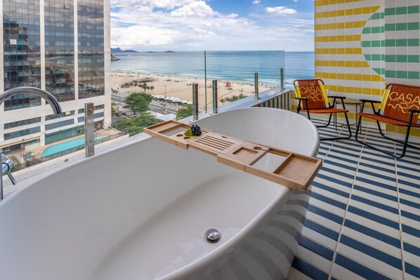 Un baño moderno con una bañera grande, una bandeja de madera y vistas a la playa y al océano.