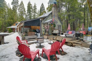 Una cabaña rústica con chimenea, asientos exteriores y una terraza cubierta de nieve.