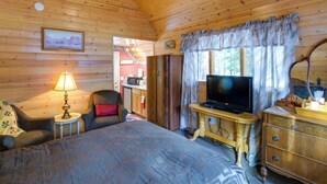 A wooden cabin room with a bed, a TV on a wooden stand, a lamp, a chair, and a small table. - Walk to Trails & Butte Creek: Cozy Retreat w/ Deck (Butte Meadows)