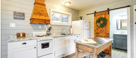 A kitchen with white cabinetry, a wooden stove, a dishwasher, a refrigerator, and a wooden table with a cutting board.