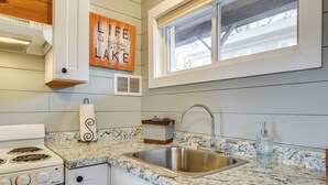 A kitchen with a stainless steel sink, white cabinets, a stove, and a window above the sink. - Hike, Boat, Fish & More: Table Rock Lake Cottage (Cape Fair)