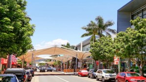 A street with parked cars, trees, and a building with a modern design.