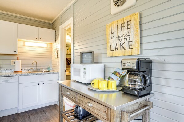 A kitchen with white cabinets, a microwave, a coffee maker, and a sign that says "Life is good at the lake".