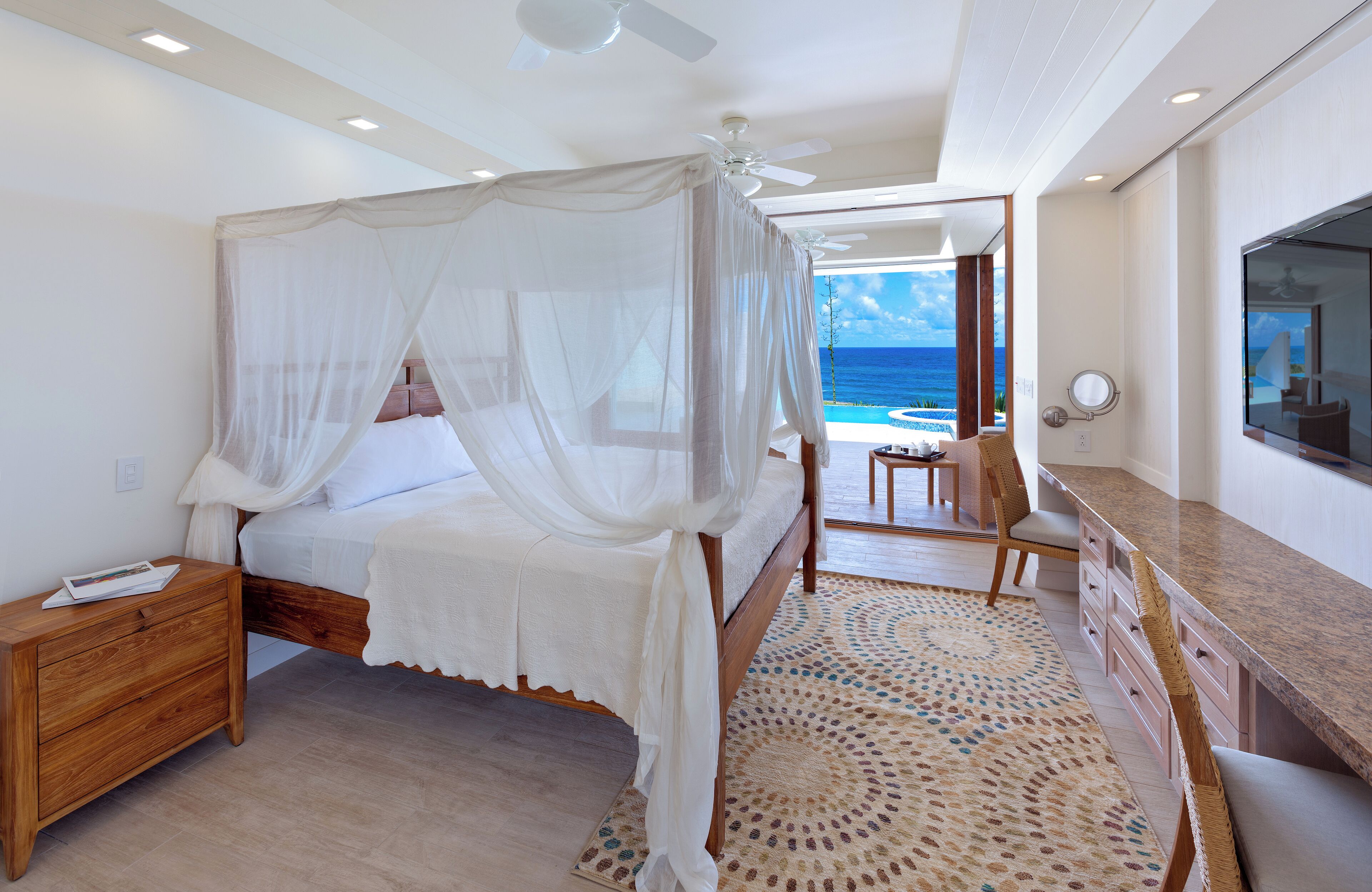 A bedroom with a bed, nightstand, and a view of the ocean.