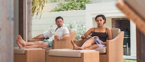 Two people seated on wicker chairs in a patio area with a brick fireplace in the background.