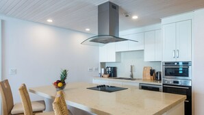 A modern kitchen with a central island, white cabinetry, stainless steel appliances, and wicker chairs.