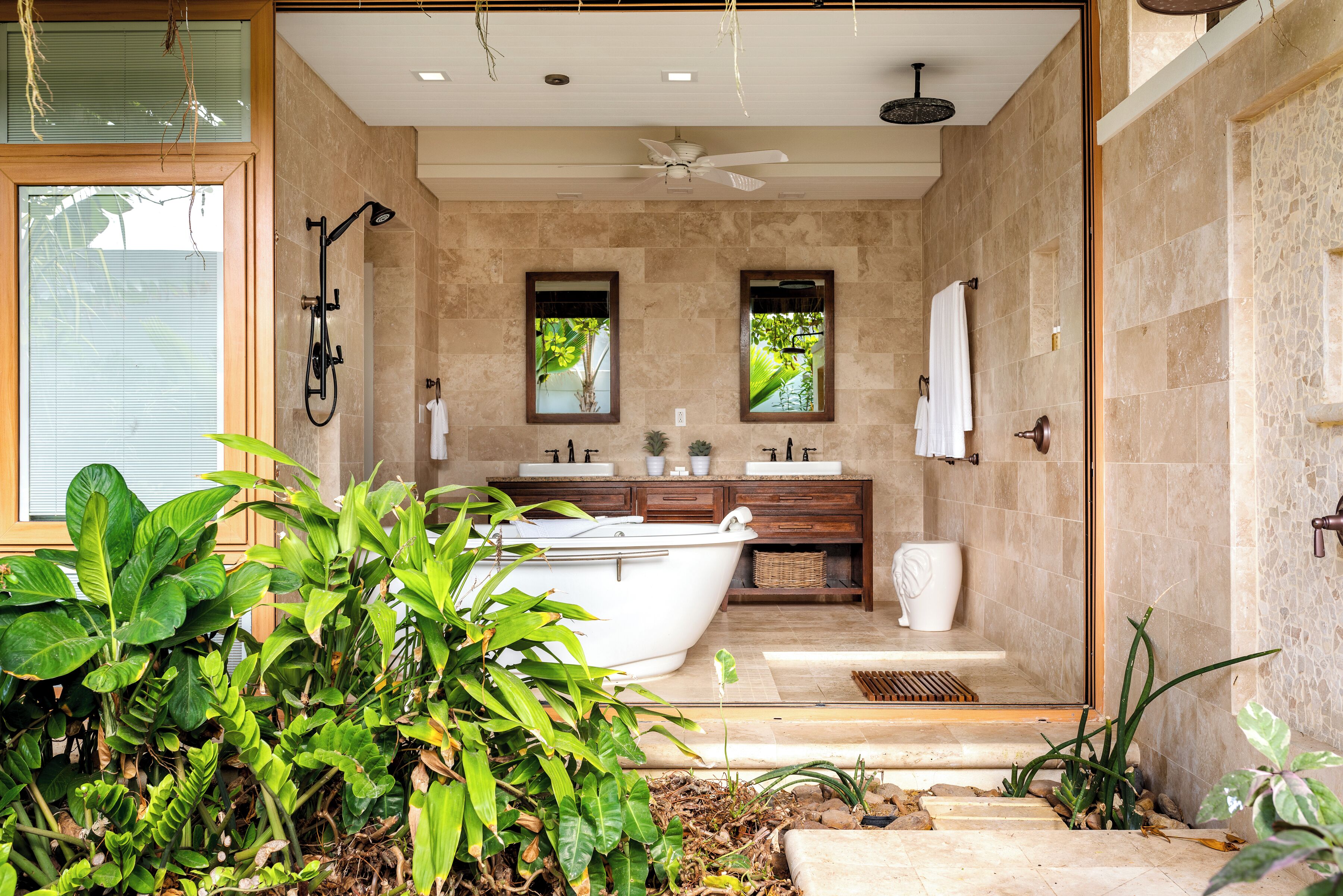 A modern bathroom with a freestanding bathtub, a ceiling fan, and a large window.