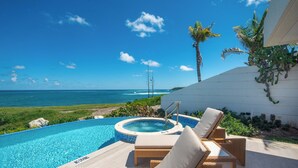 A poolside area with lounge chairs and a hot tub overlooking the ocean.
