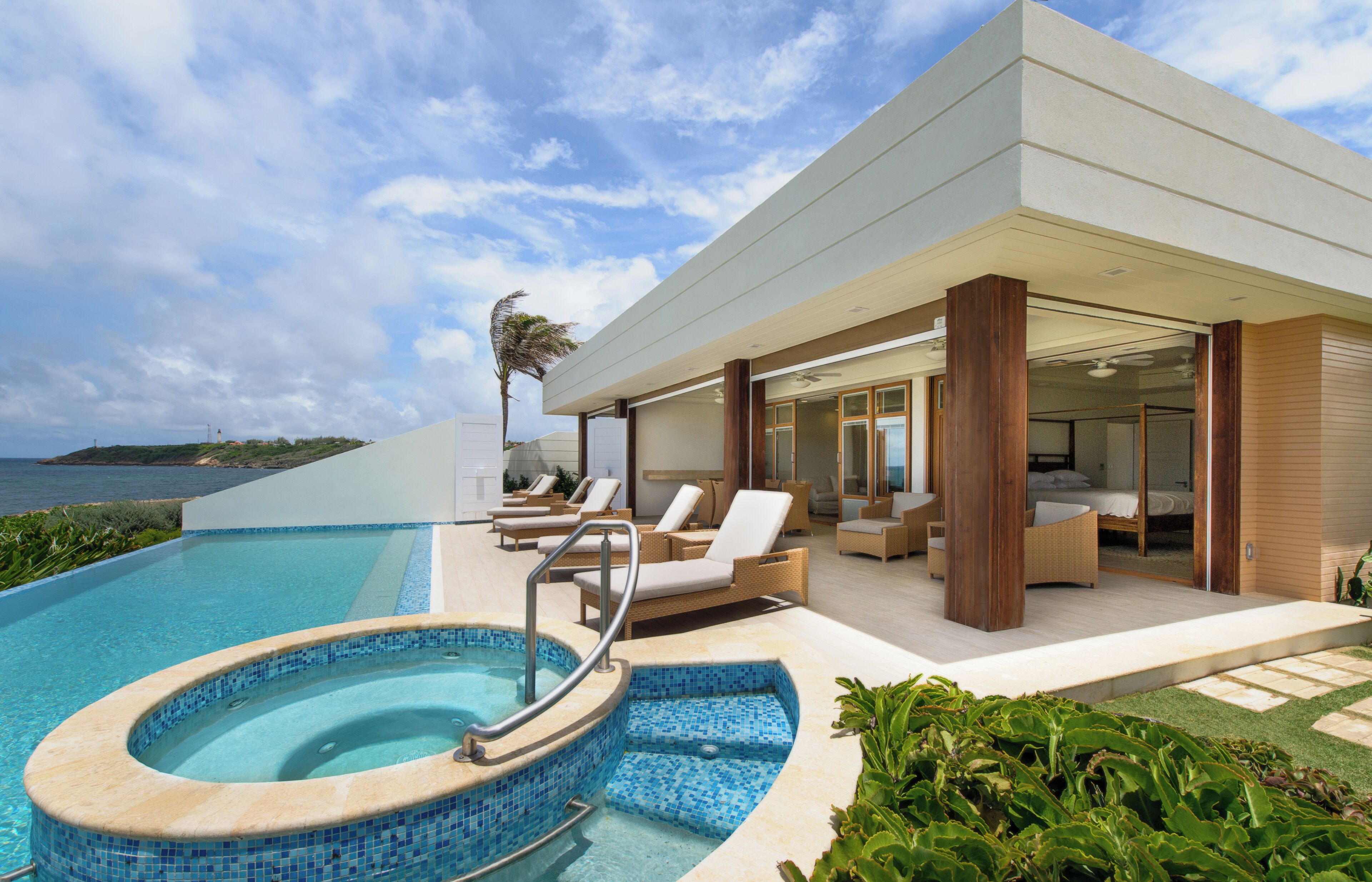 A modern resort with a swimming pool, lounge chairs, and a view of the ocean.