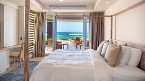 A hotel room with a large bed, a desk, and a view of the ocean. - East Resort (St. Phillips)