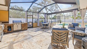 Une terrasse extérieure couverte, dotée d’un espace barbecue, de sièges et offrant une vue sur une piscine.