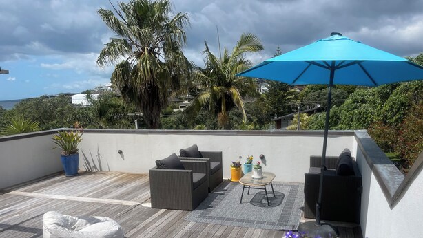 Une terrasse sur le toit, aménagée avec du mobilier d’extérieur, un parasol bleu et des plantes en pot.