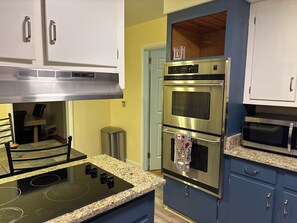 Cucina con cappa in acciaio inox, forni doppi, forno a microonde, piani di lavoro in granito e pensili bianchi.