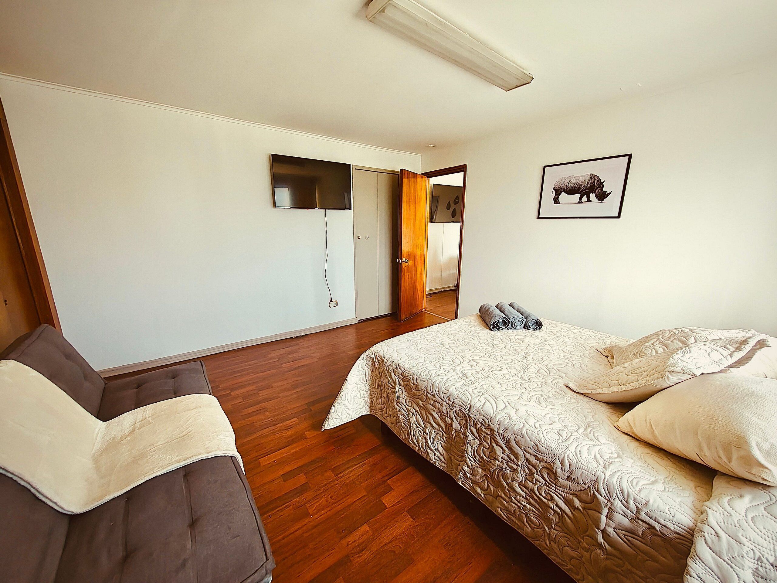 A bedroom with a bed, a chair, a wardrobe, a mirror, and a television.
