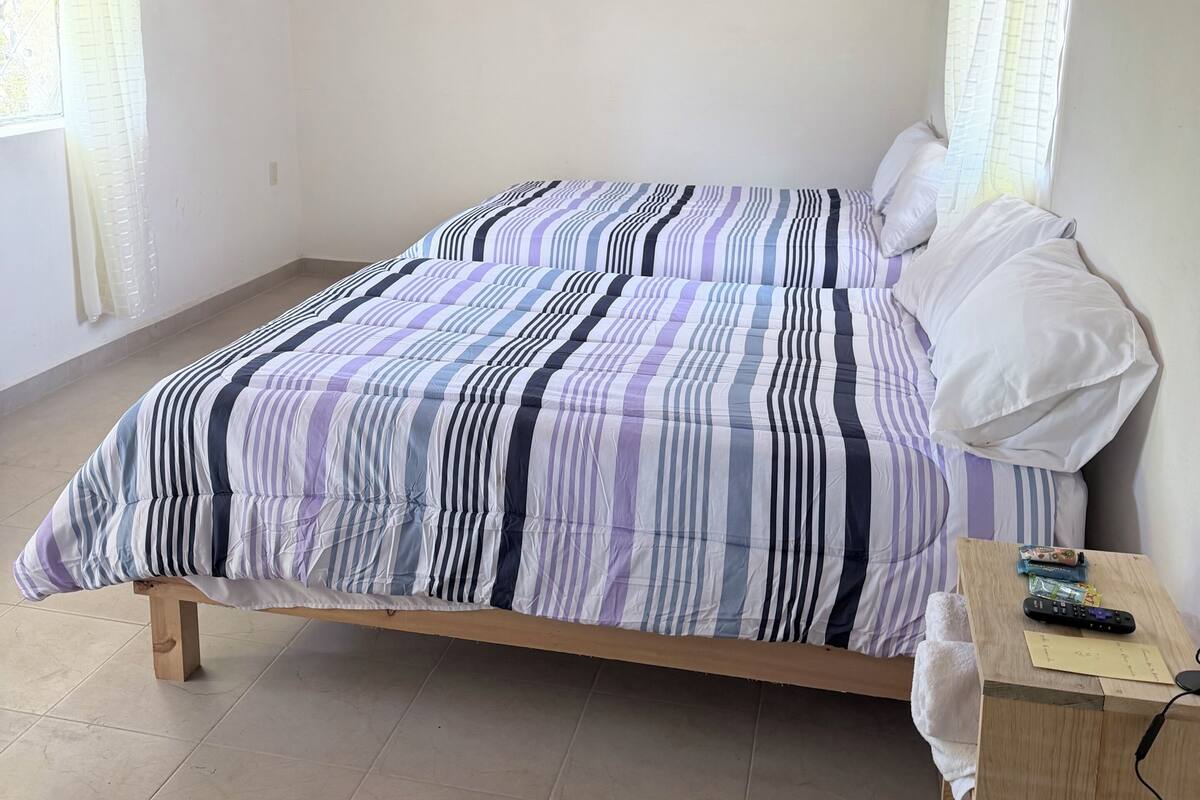 Un dormitorio con una cama, una mesita de noche de madera, un televisor de pared y un cuadro.