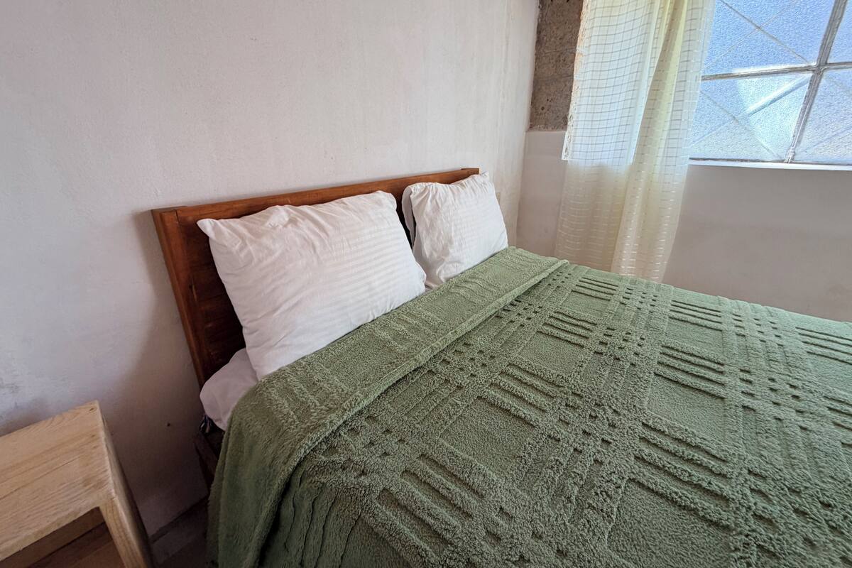 Una cama con cabecera de madera, dos almohadas blancas y una manta verde.