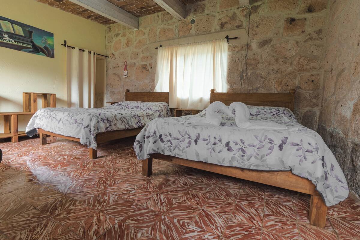 Una habitación con dos camas de madera, paredes de piedra, suelo de baldosas y un cuadro en la pared.